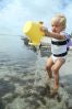 Mädchen spielt im Wasser mit gelben Scrunch Eimer von Mami Poppins und SwimFin Schwimmhilfe am Rücken